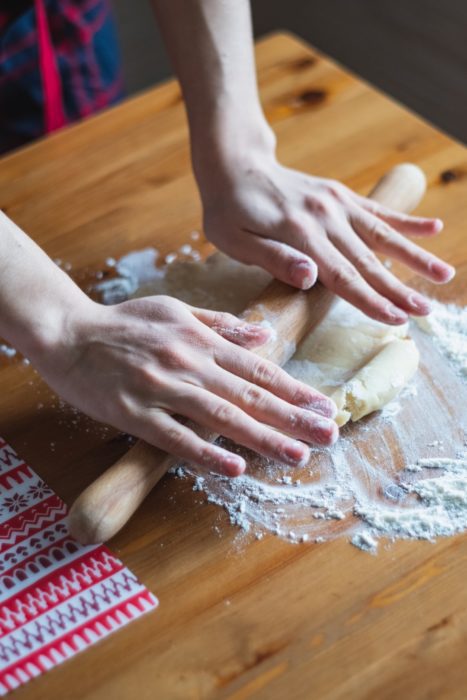 two hands roll pie dough on a cutting board